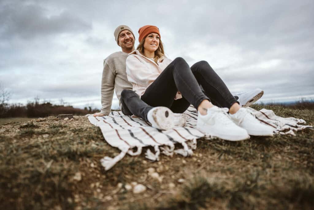 Komfortable outdoor-szene mit einem paar, das auf einer decke im freien sitzt und die natur genießt, stimmung mit bewölktem himmel und herbstkleidung, ideal für lifestyle und outdoor-aktivitäten, inklusive schlüsselewort-suche nach lieblingsbeschäftigungen im freien.